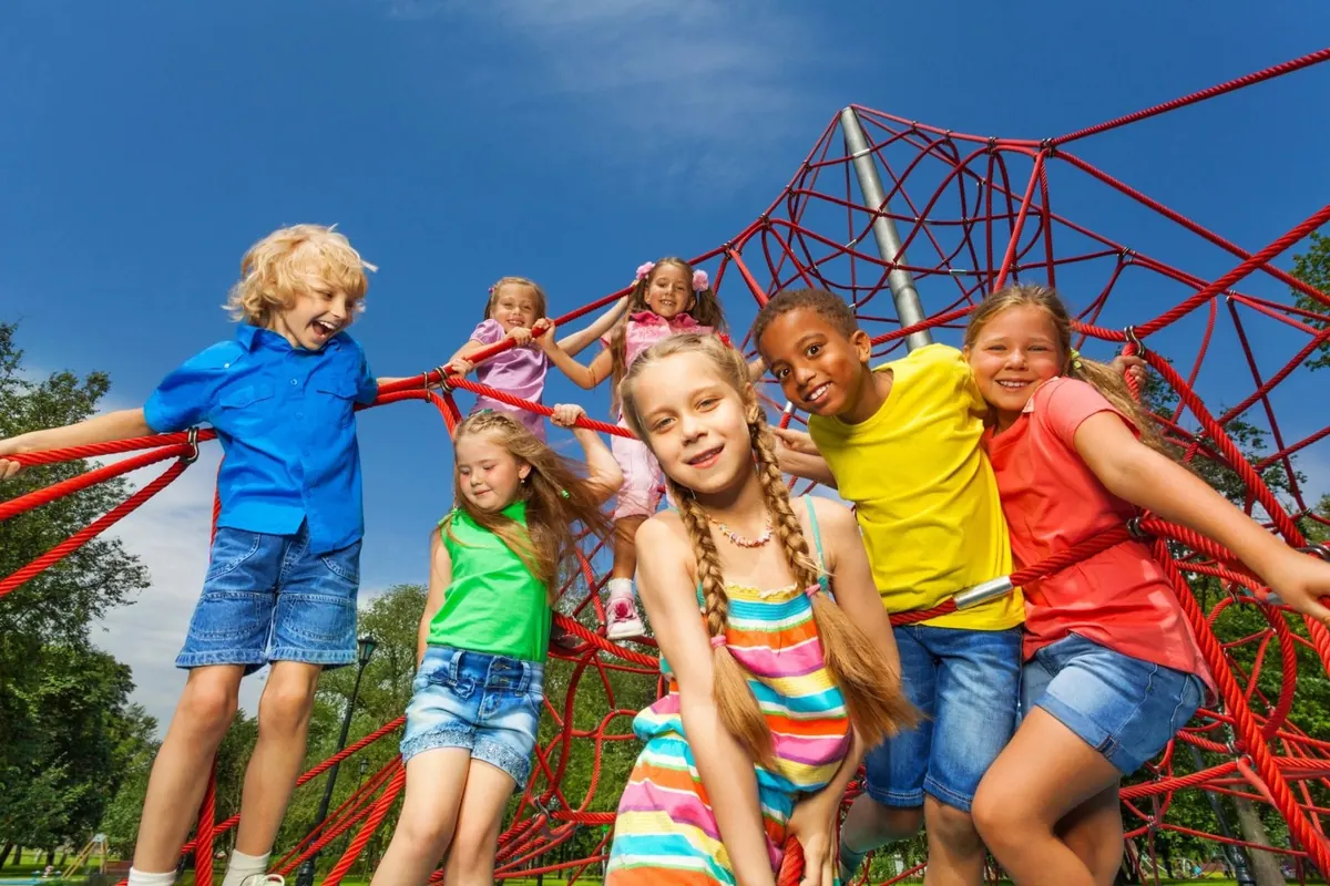 Children smiling and climbing on a red rope playground structure.
