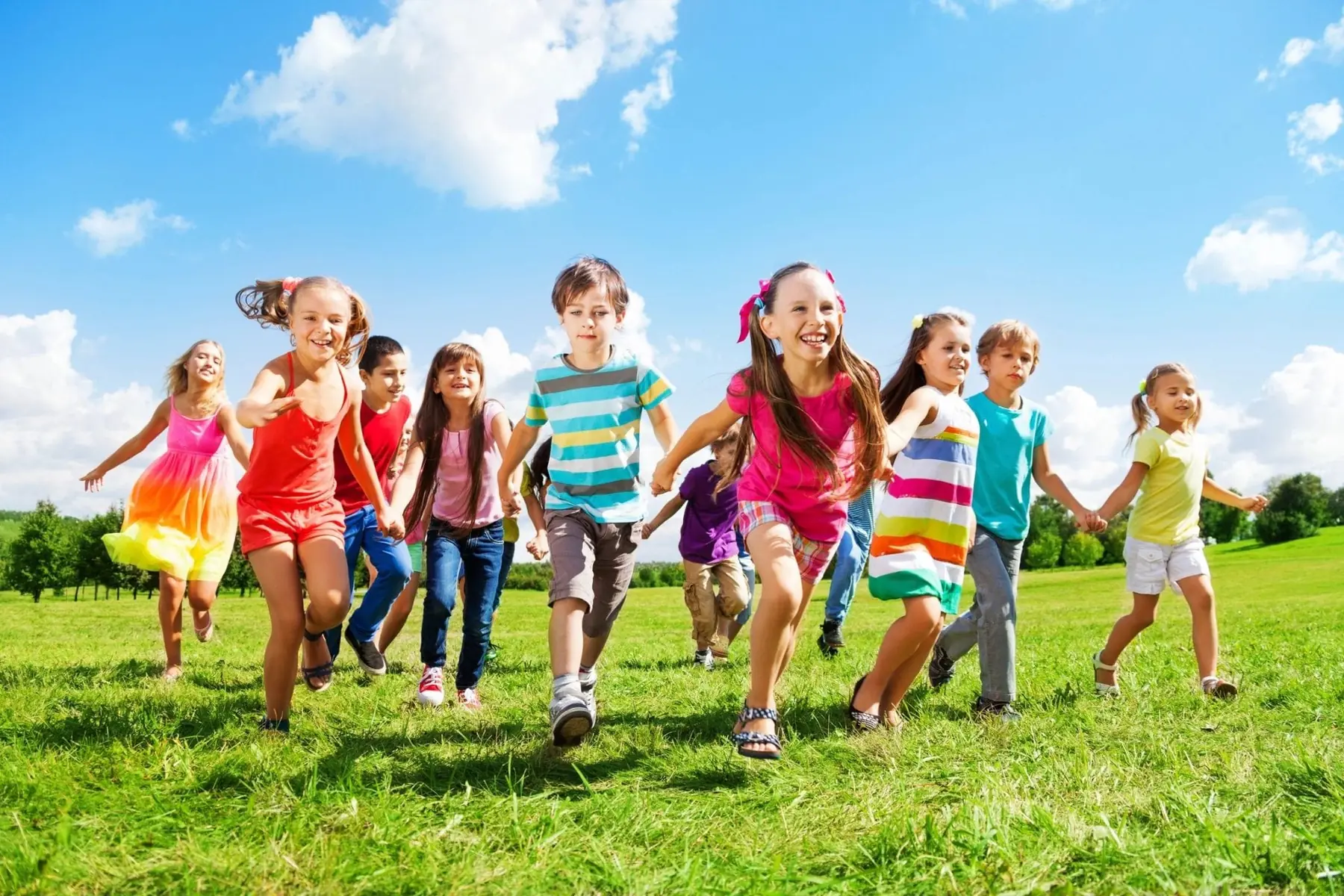 Children holding hands and running across a sunny green field.