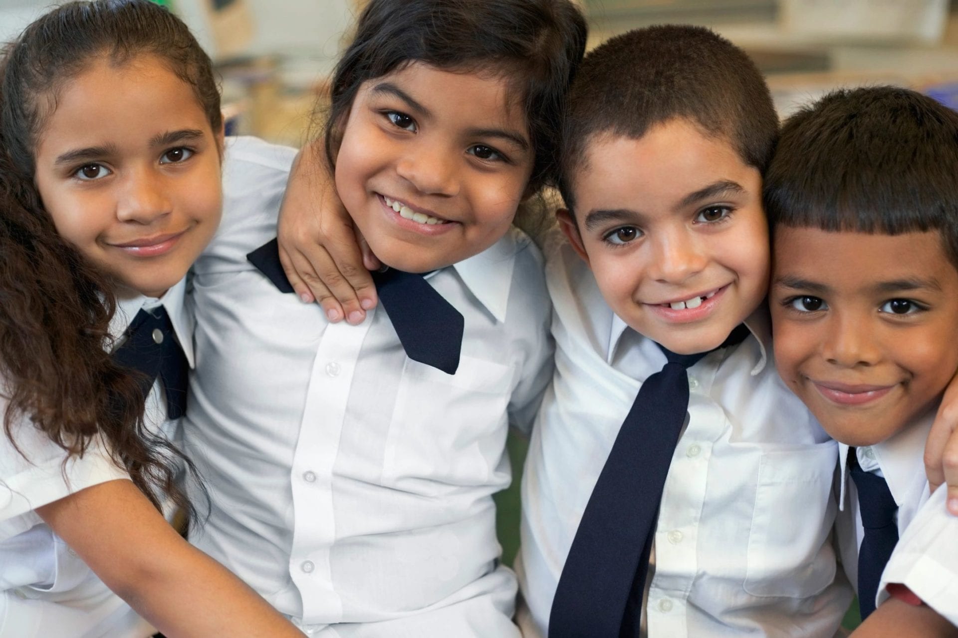 Four smiling schoolchildren in white shirts and navy ties with their arms around each other.