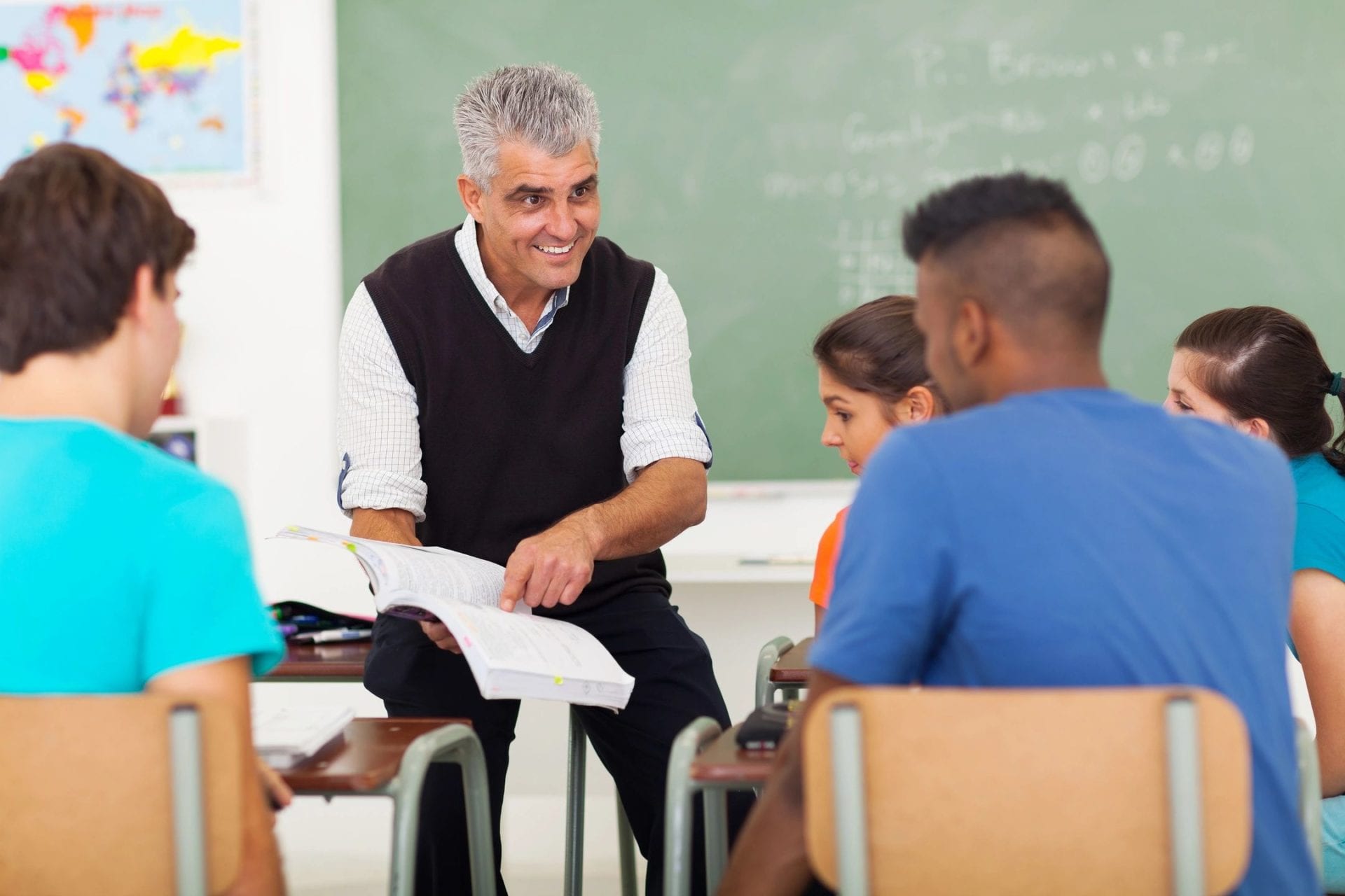 A teacher smiles and shows an open book to students in a classroom.